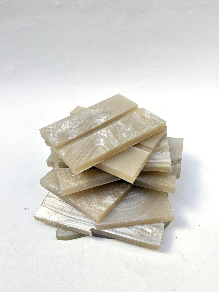 A stack of rectangular translucent resin or acrylic tiles in warm beige and cream tones with natural marbled swirls, photographed on a plain white studio background.